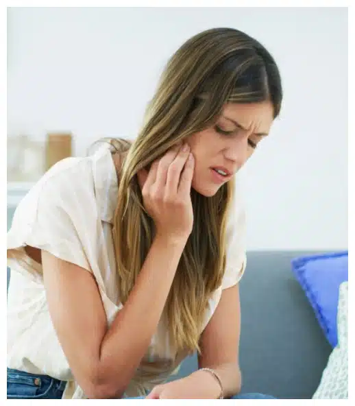 Woman with tooth pain holding cheek, appearing uncomfortable in dental office setting.