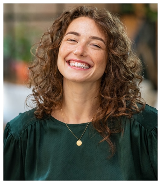 Smiling woman with curly brown hair wearing green shirt in professional dental office portrait.