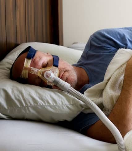 Patient sleeping peacefully in bed wearing oral sleep apnea device mask.