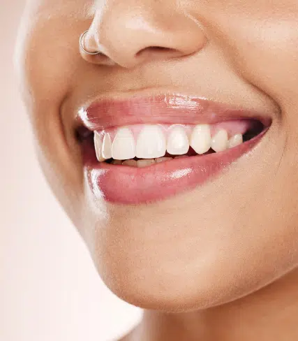 Close-up of person smiling, displaying bright white teeth and healthy gums against neutral background.