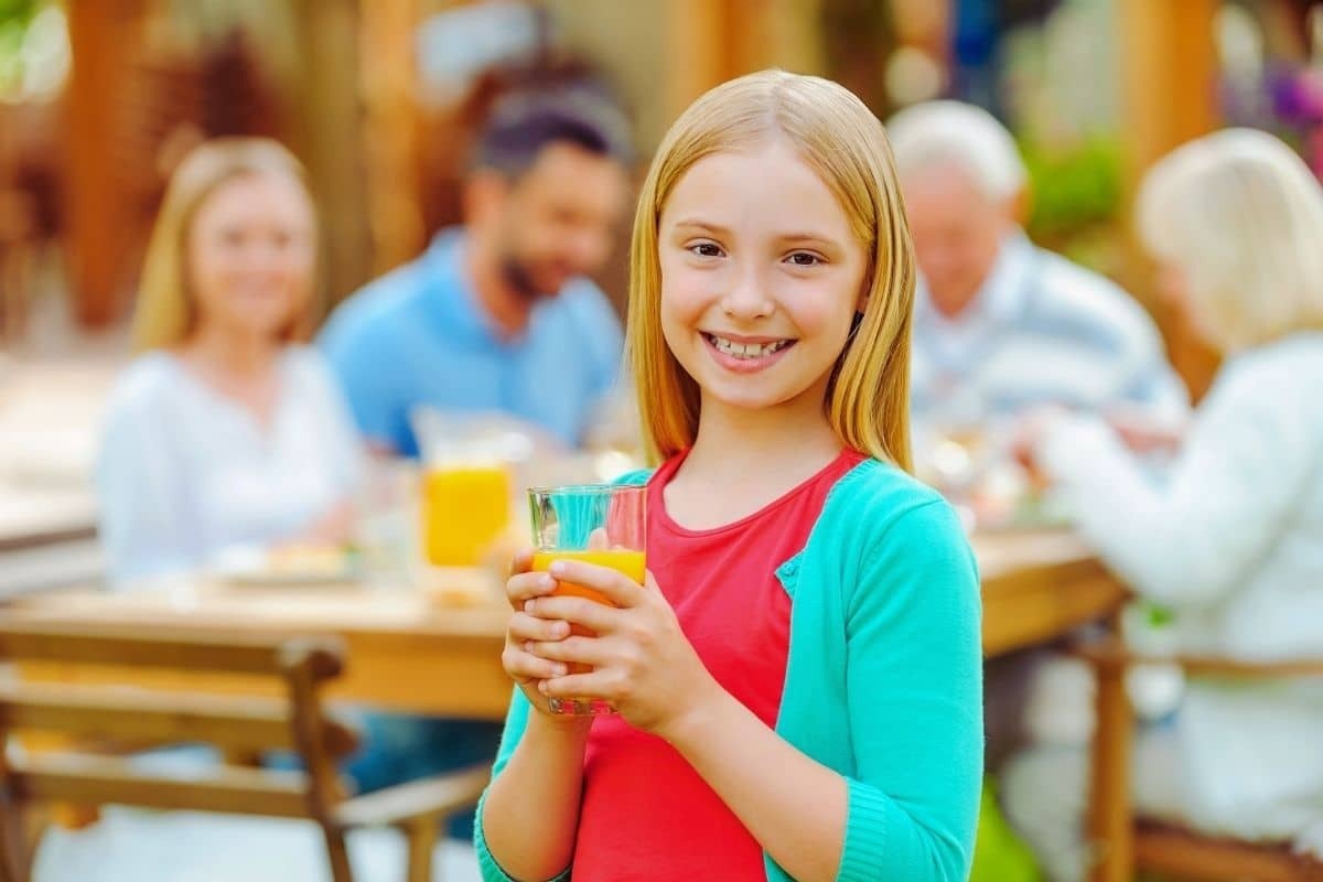 A young girl with a bright smile holds a glass of orange juice.