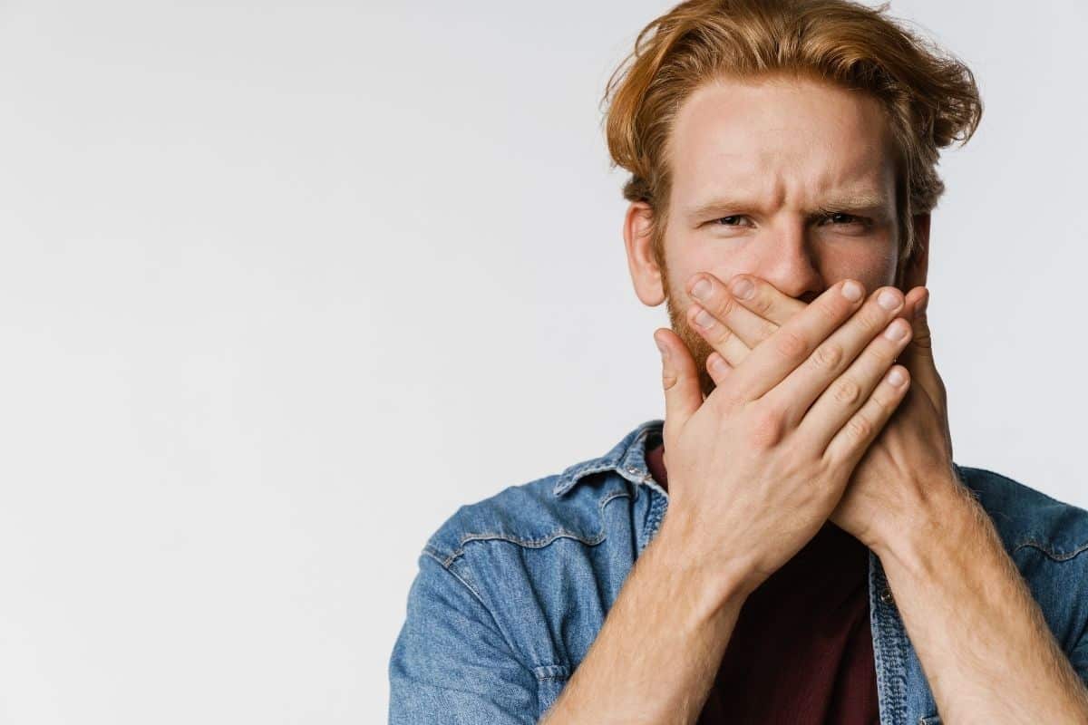 Man hiding his mouth emphasizing dental causes for metalic taste in the mouth